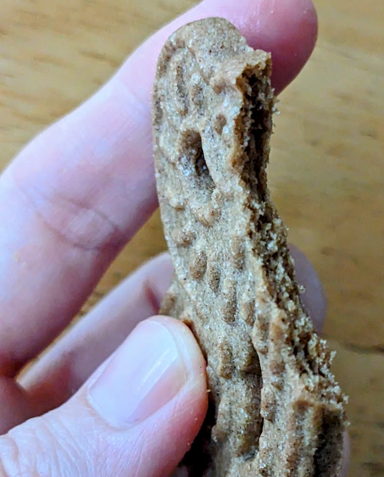 Fingers holding a bitten Aldi Spekulatius cookie over a wooden table.