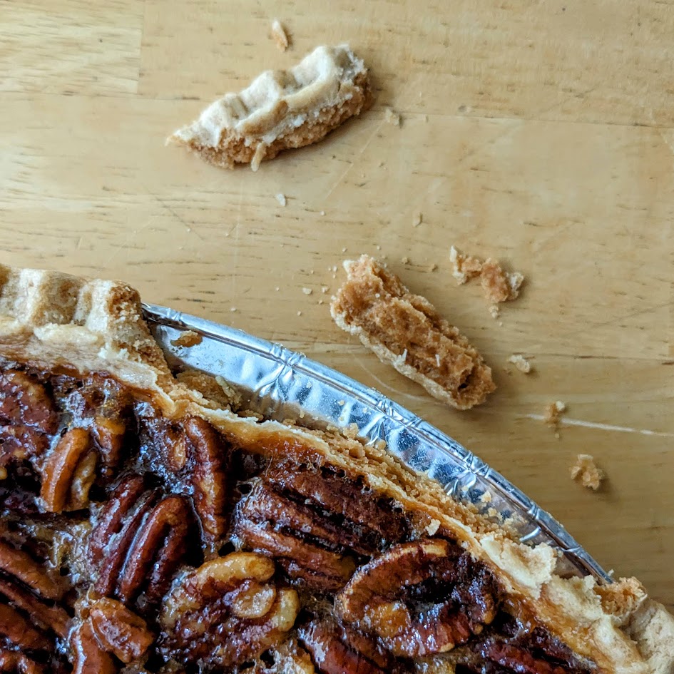 Broken pie crust along the rim of an aluminum pan holding a Costco pecan pie.