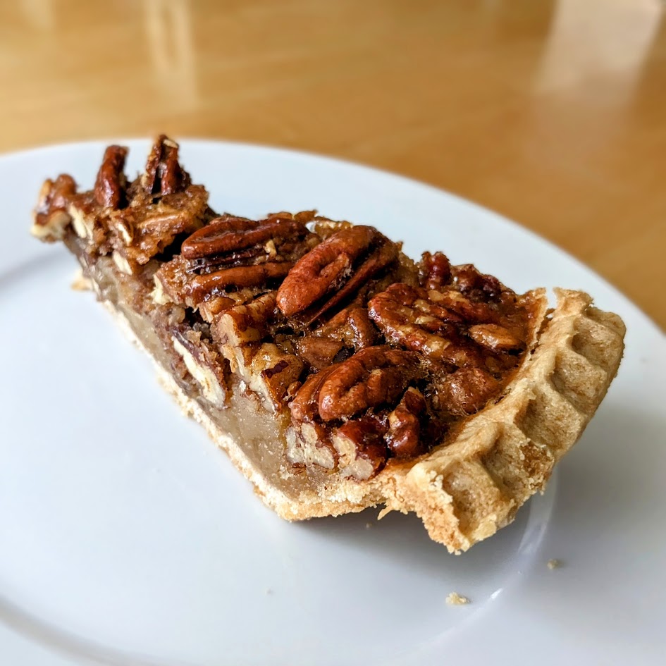 A slice of Costco Pecan Pie, sitting on a small white plate.