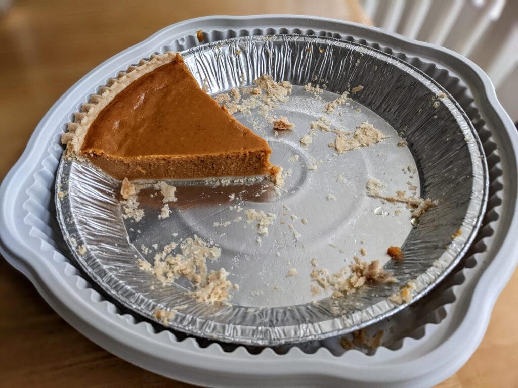 A single slice of Costco's Kirkland Pumpkin Pie, sitting in an empty metal pie pan on a table.