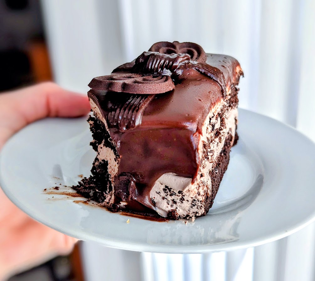 A hand holding a white plate with a slice of Publix Bakery chocolate ganache supreme cake.