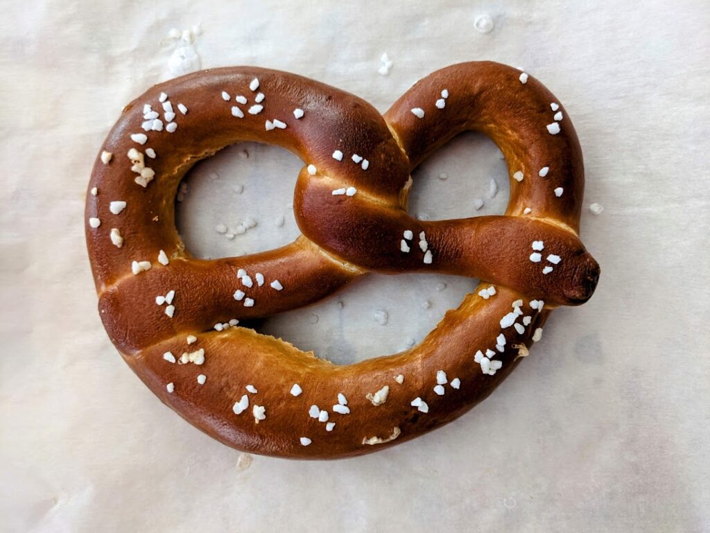 A baked Bavarian Soft Pretzel, sitting on white parchment paper, from Aldi's Deutsche Kuche German Week brand.