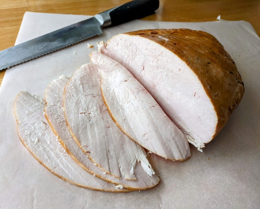 A sliced turkey breast from Costco, sitting on white parchment with a serrated knife.