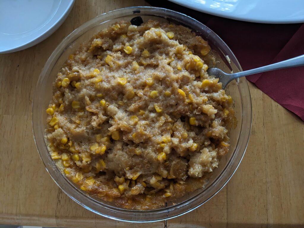 Publix Corn Casserole, in a glass baking dish with a spoon, on a kitchen table.