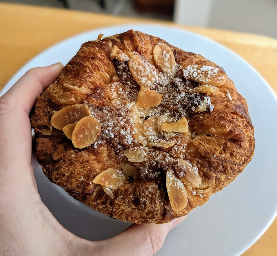 A hand holding a large Costco Almond Croissant Pastry.