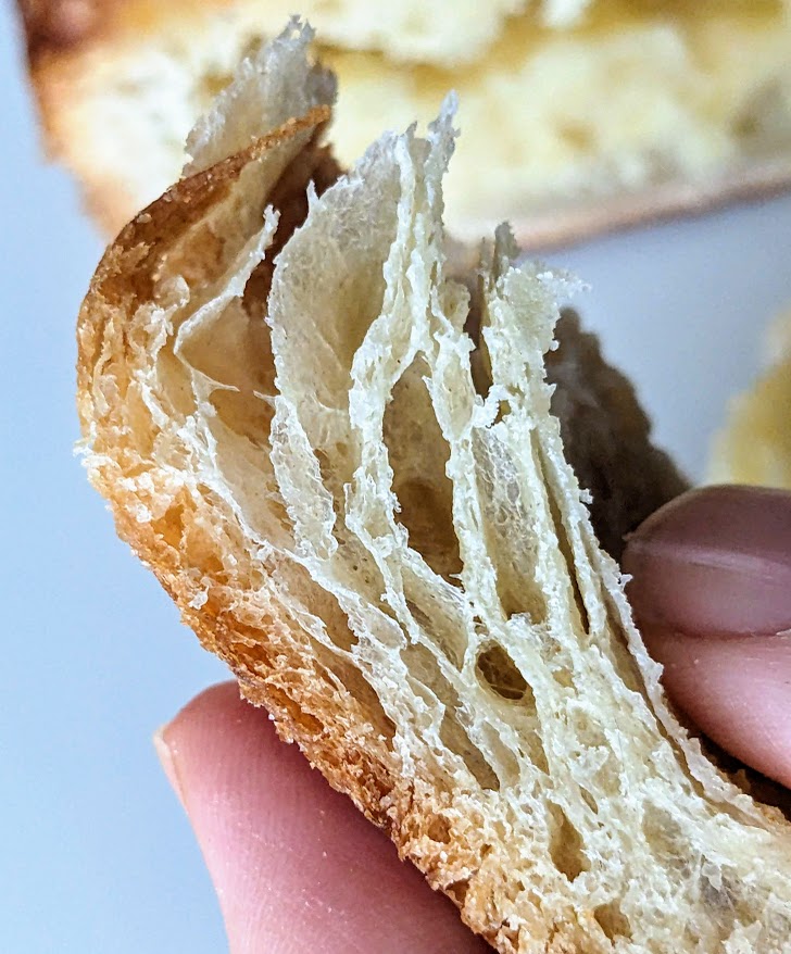 Fingers holding pastry layers from an Almond Croissant from Costco Bakery.