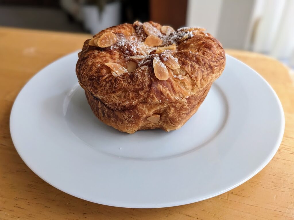 A muffin-shaped Almond Croissant from Costco, sitting on a white plate.