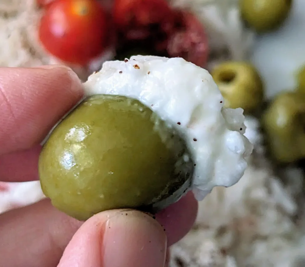 Fingers holding a green olive dipped in TOOM garlic sauce.
