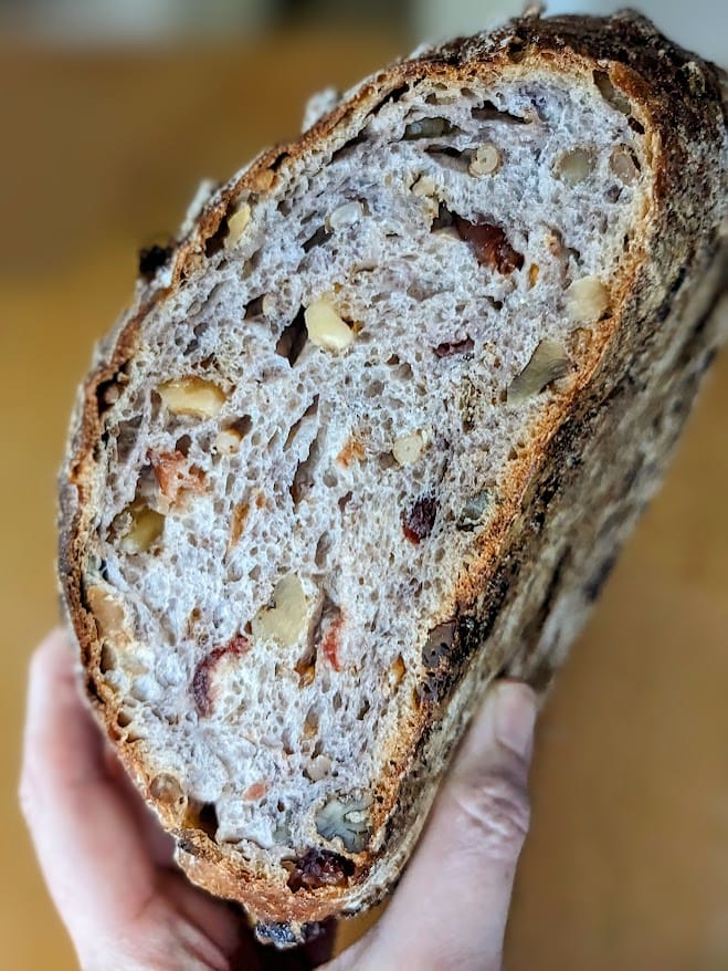 A hand holding a sliced loaf of Cranberry Walnut Bread from Costco bakery.