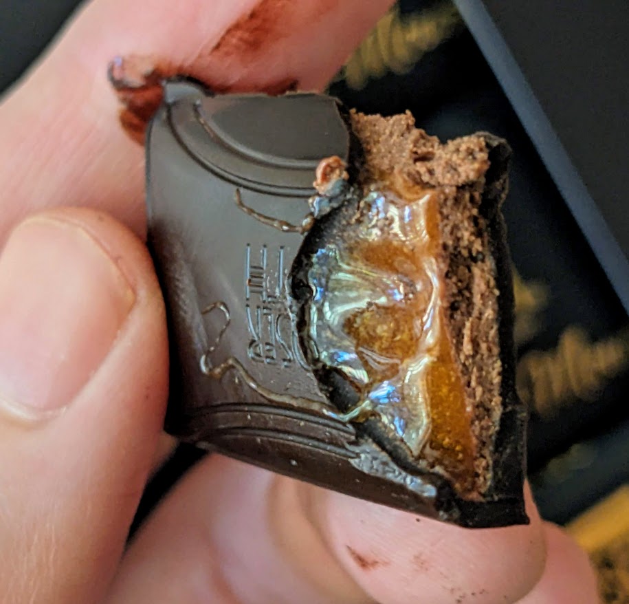 Fingers holding a bitten segment of an Aldi Dark Chocolate Orange Mousse bar from Aldi.