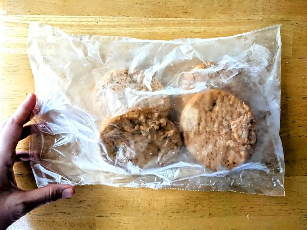 A hand holding a plastic bag of four frozen salmon burger patties from Aldi.