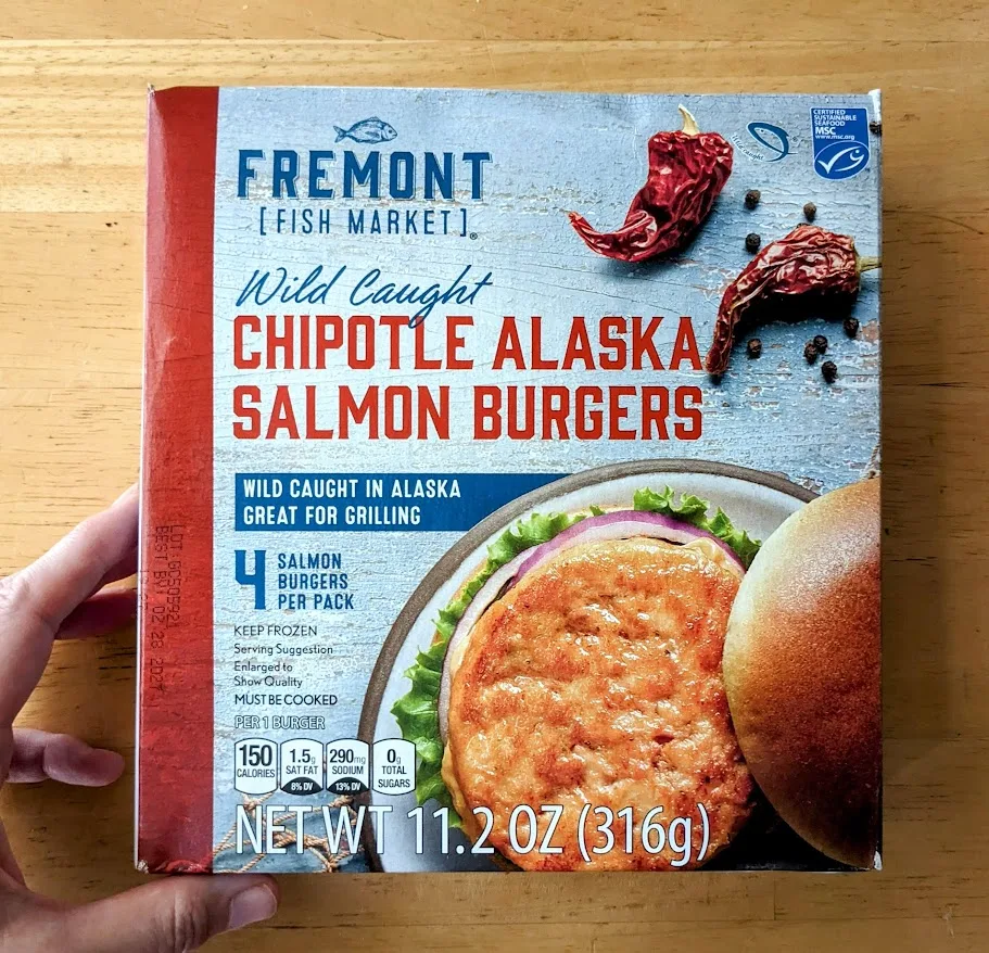 A hand holding a box of frozen Wild Caught Chipotle Alaska Salmon Burgers from Aldi.