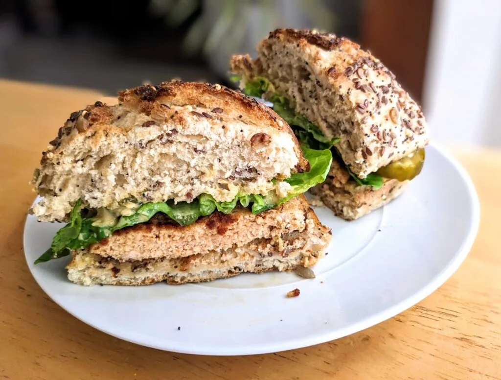 A white plate with two halves of a sandwich made with Aldi Chipotle Salmon Burger, sourdough bun, and artisan lettuce.