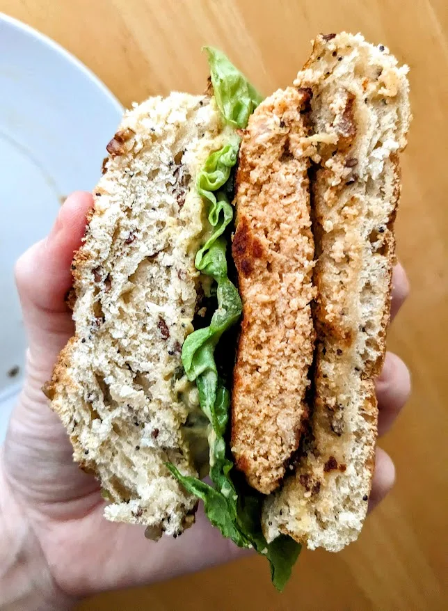 A hand holding half a sandwich made with an Aldi Chipotle Salmon Burger from Fremont store brand.
