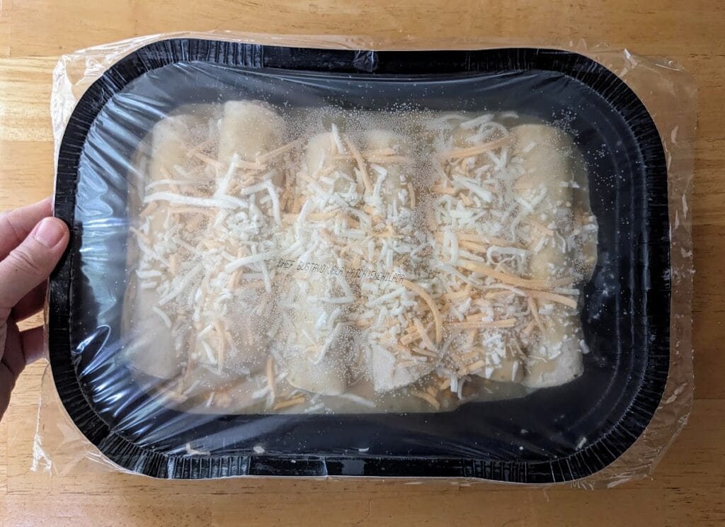 A hand holding a frozen cardboard tray of Chef Gustavo Chicken and Cheese Enchiladas.