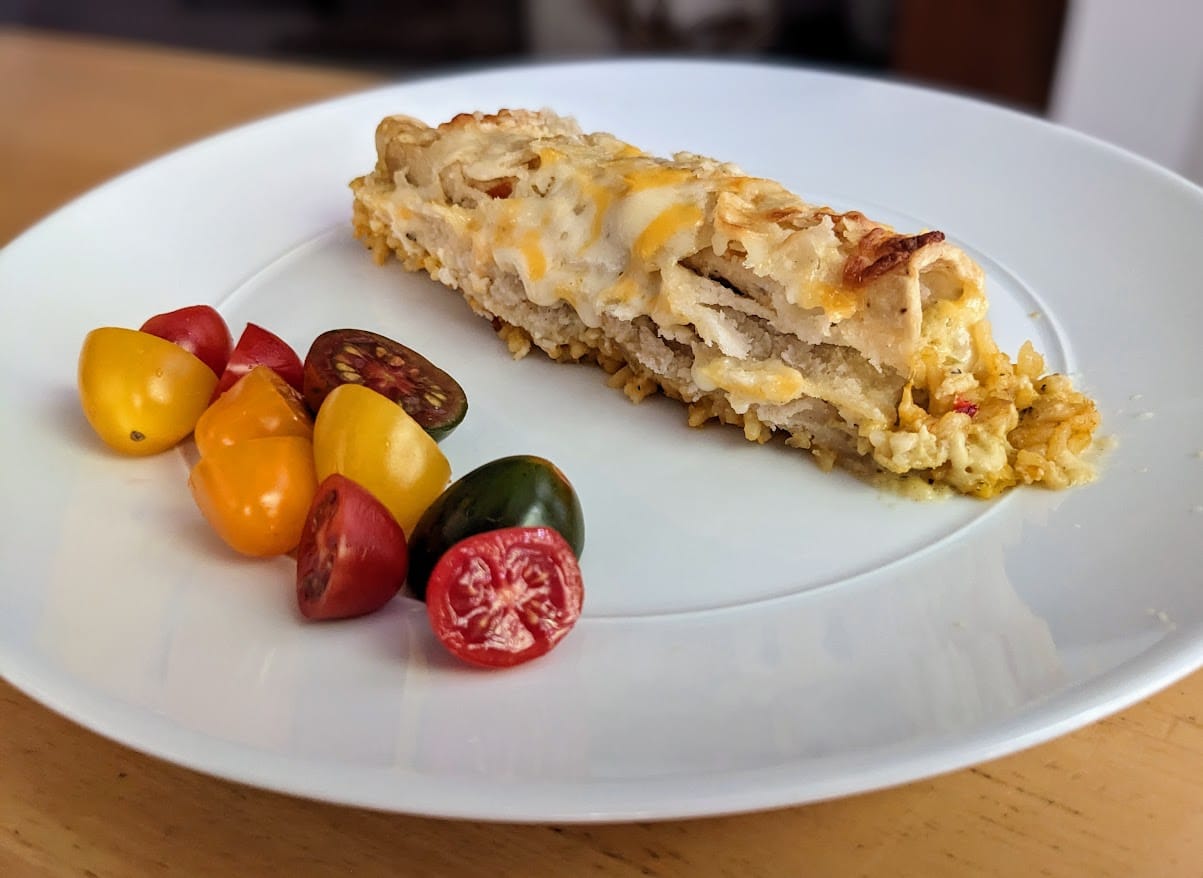 A white plate with one Chef Gustavo Chicken and Cheese Enchilada with sliced tomatoes, sitting on a kitchen table.