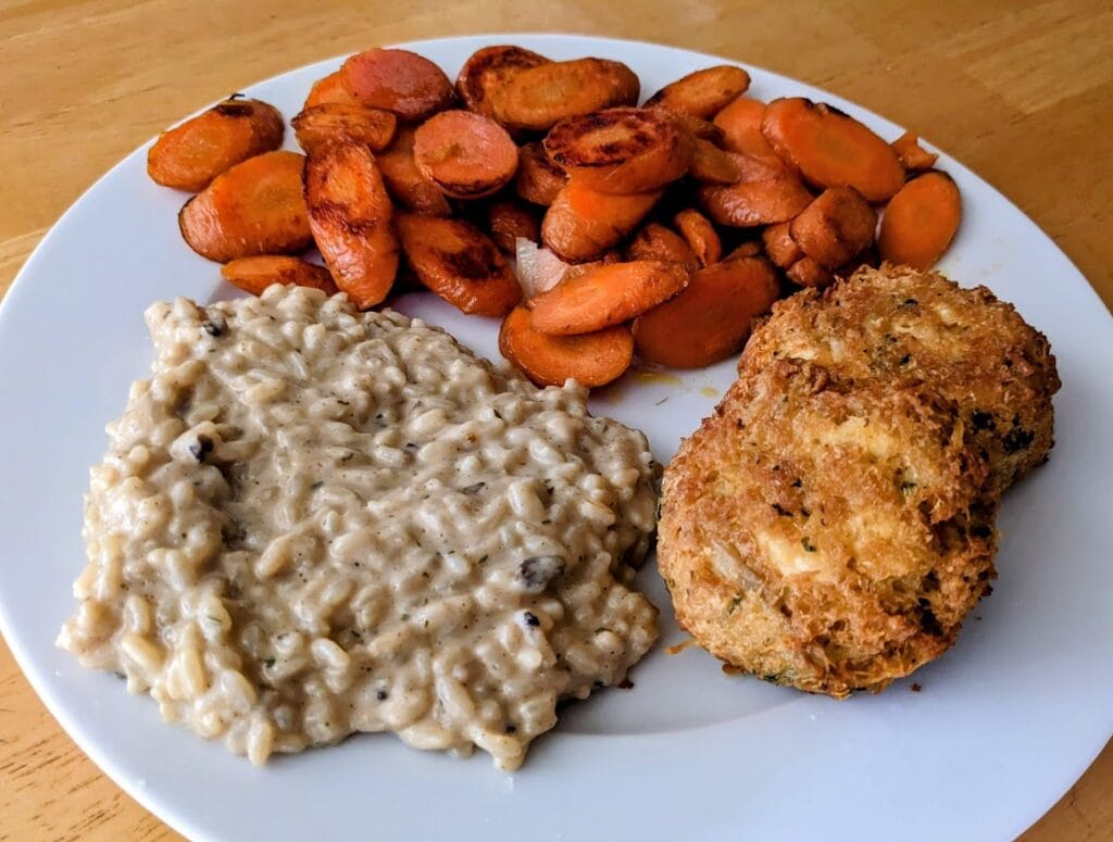Aldi Priano Mushroom Risotto on a dinner plate with two crab cakes and a pile of sauteed carrots.