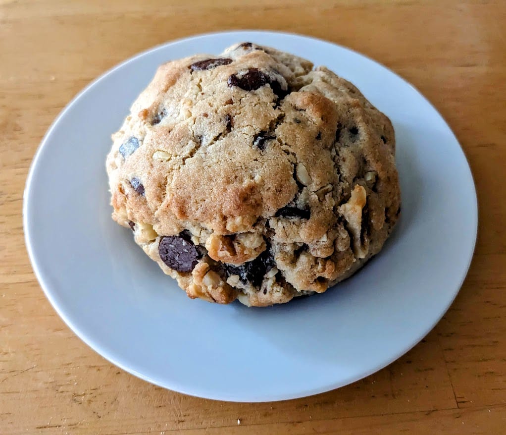 A large chocolate walnut Levain-style cookie, sitting on a small white plate.