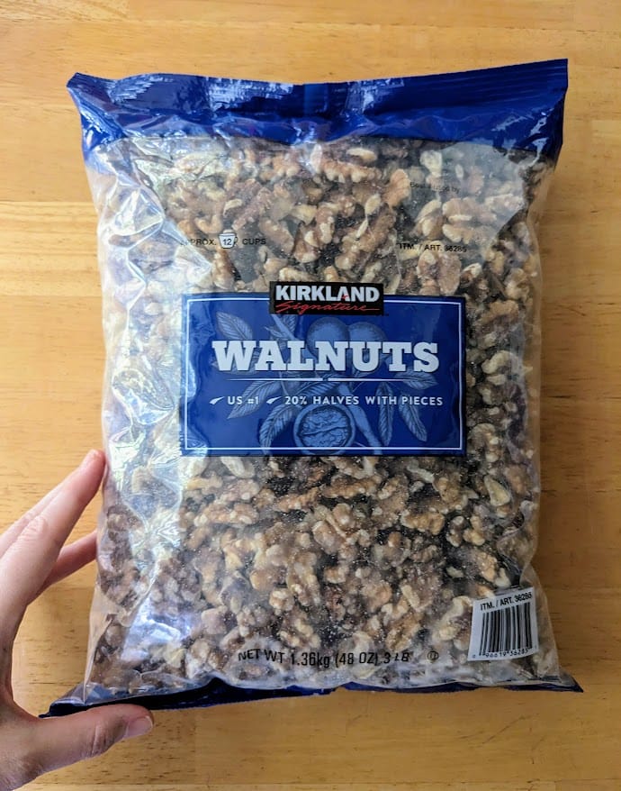 A hand holding a 3-pound bag of Costco Kirkland Walnut Halves.