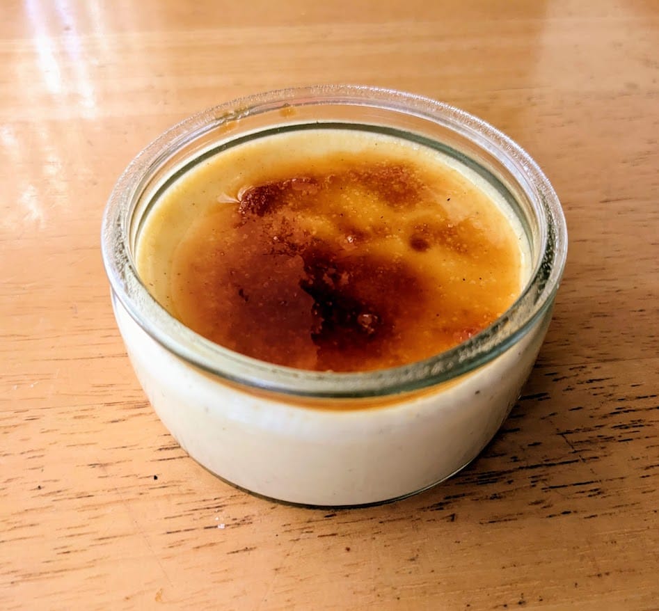 A glass dish of broiled Senoble French Creme Brulee from Costco sitting on a kitchen table.