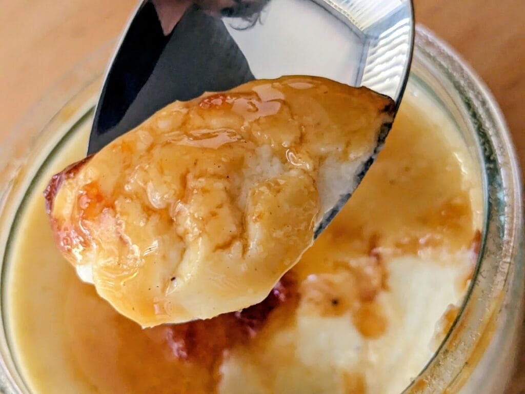 A spoon holding a bite of Senoble French Creme Brulee with caramelized sugar on top.