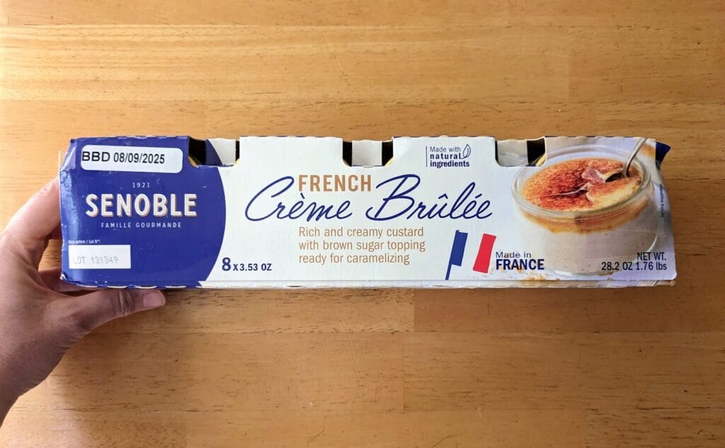 A hand holding a long package of single-serve Senoble French Creme Brulee from Costco.