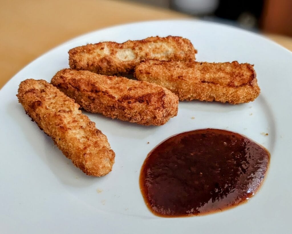 Fish sticks on a white plate with a small puddle of Burman's Kansas City BBQ Sauce from Aldi.