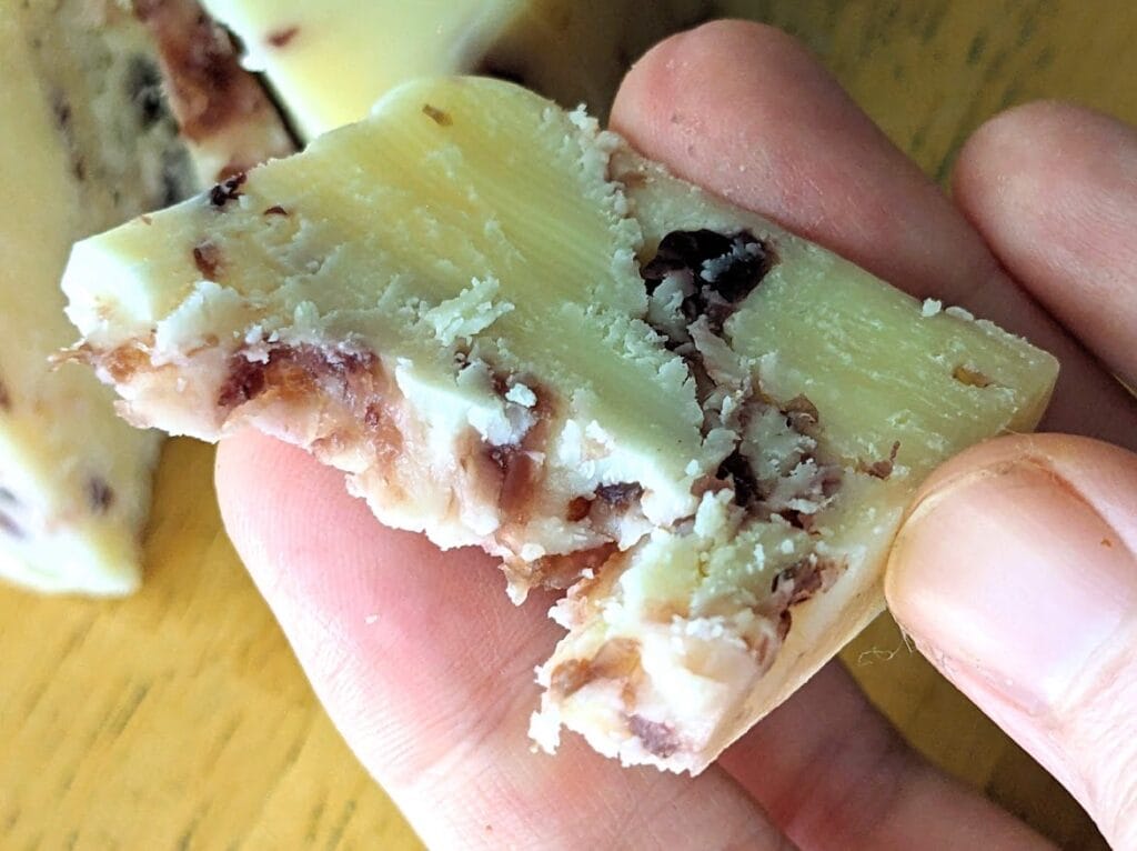 Fingers holding a bitten piece of Cranberry White Cheddar Cheese from Aldi.