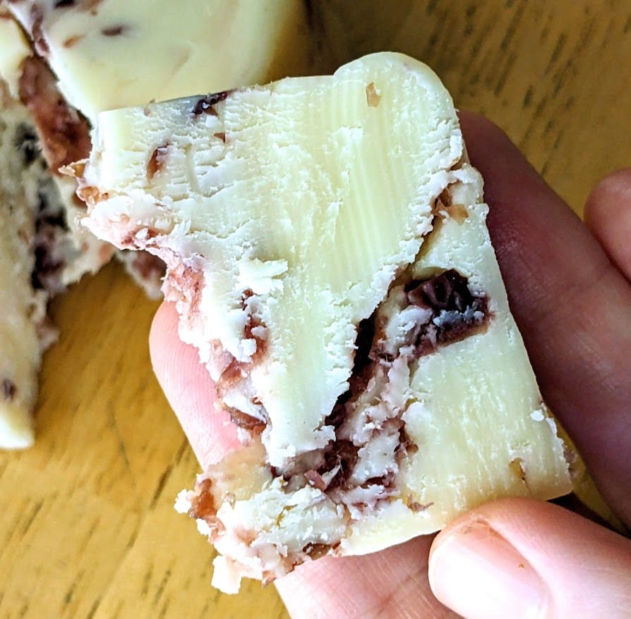 Fingers holding a slice of Cranberry White Cheddar cheese from Aldi Emporium Selected brand.