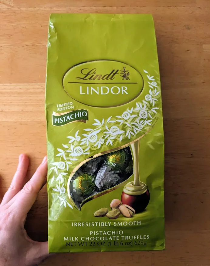 A hand holding a bag of Lindt Pistachio Milk Chocolate Truffles from Costco.