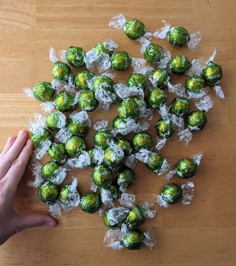 A hand next to a pile of wrapped Lindt Pistachio Truffles from Costco.