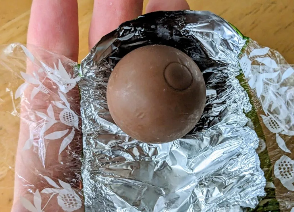 A hand holding an unwrapped Lindt Lindor Milk Chocolate Pistachio Truffle.