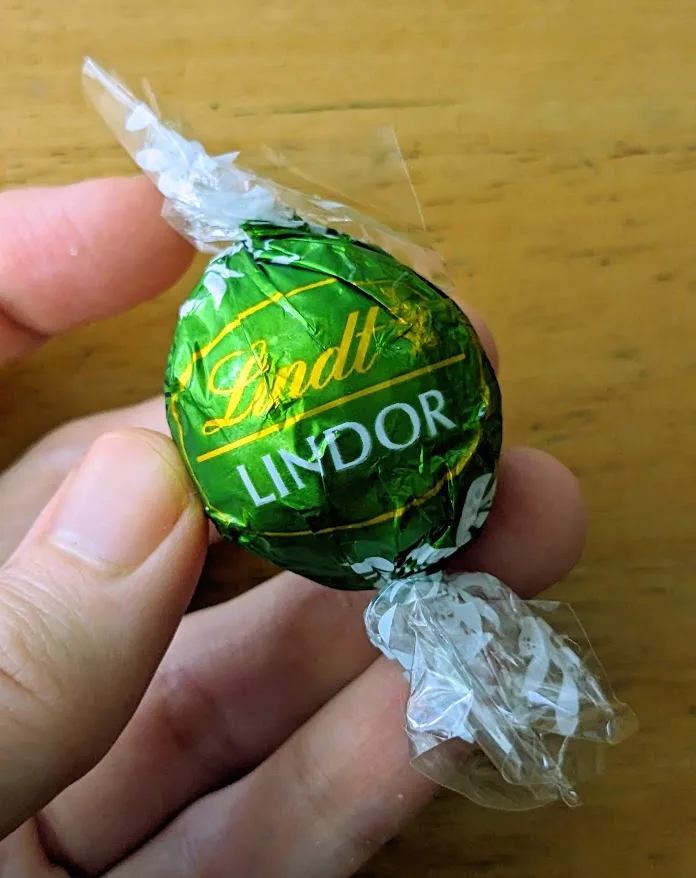 Fingers holding a green wrapped Lindt Lindor Pistachio Truffle candy.
