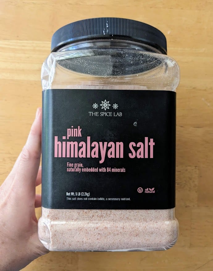A hand holding a 5 pound plastic jug of Pink Himalayan Salt from Costco.