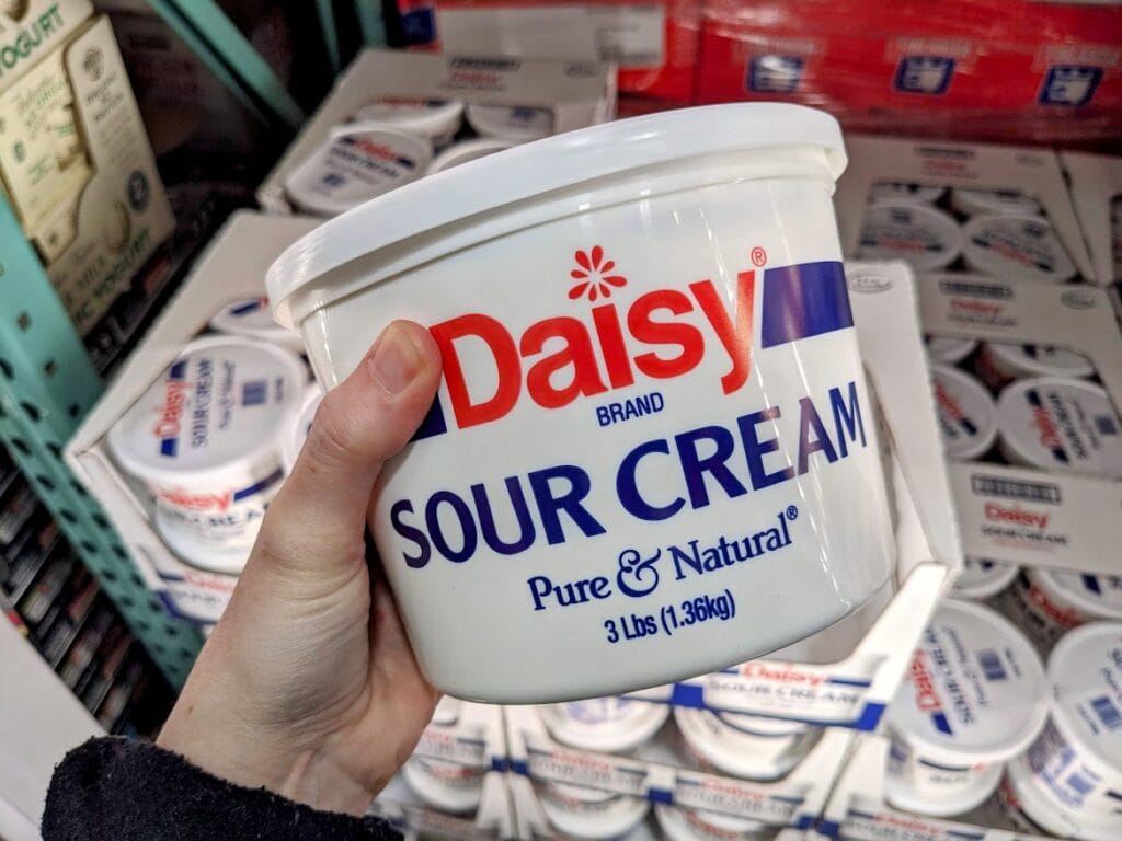 A hand holding a 3-pound tub of Daisy Sour Cream from Costco.