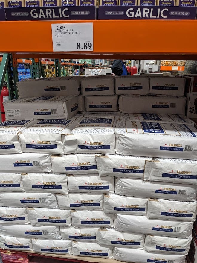 Shelves stacked with Ardent Mills 25 pound bags of All Purpose Flour inside a Costco Warehouse.