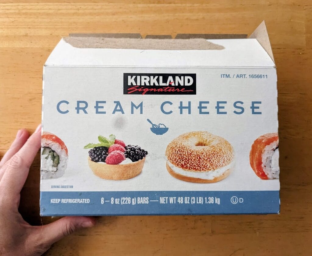 A hand holding a Kirkland Cream Cheese 3-pound box from Costco.