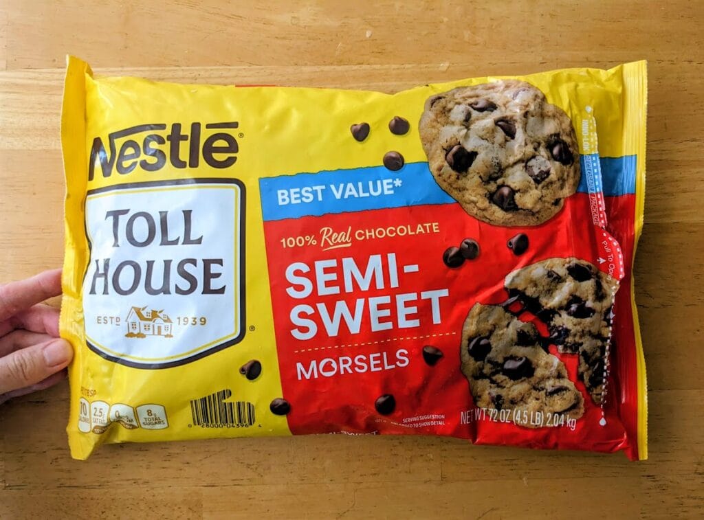 A hand holding a 72 ounce bag of Nestle Toll House Semi-Sweet Chocolate Chips from Costco.