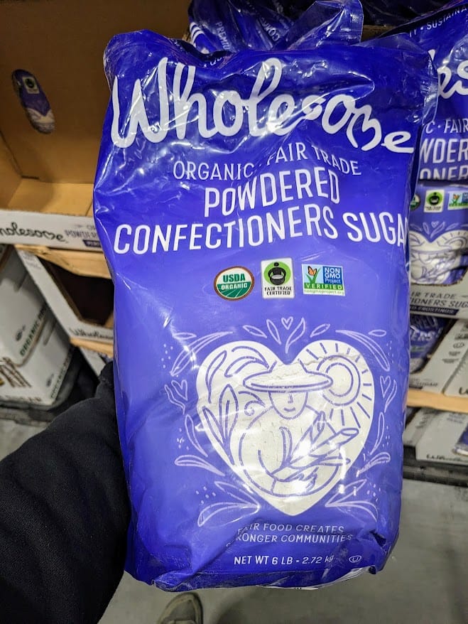 An arm holding a 6 pound bag of Wholesome Organic Fair Trade Powdered Confectioners Sugar from Costco.