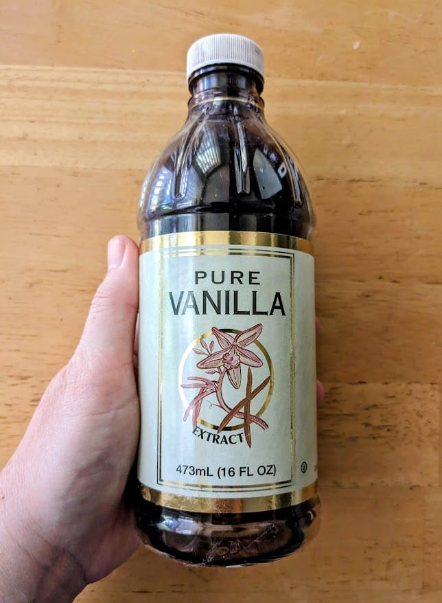 A hand holding a 16 ounce bottle of Pure Vanilla extract from Costco.
