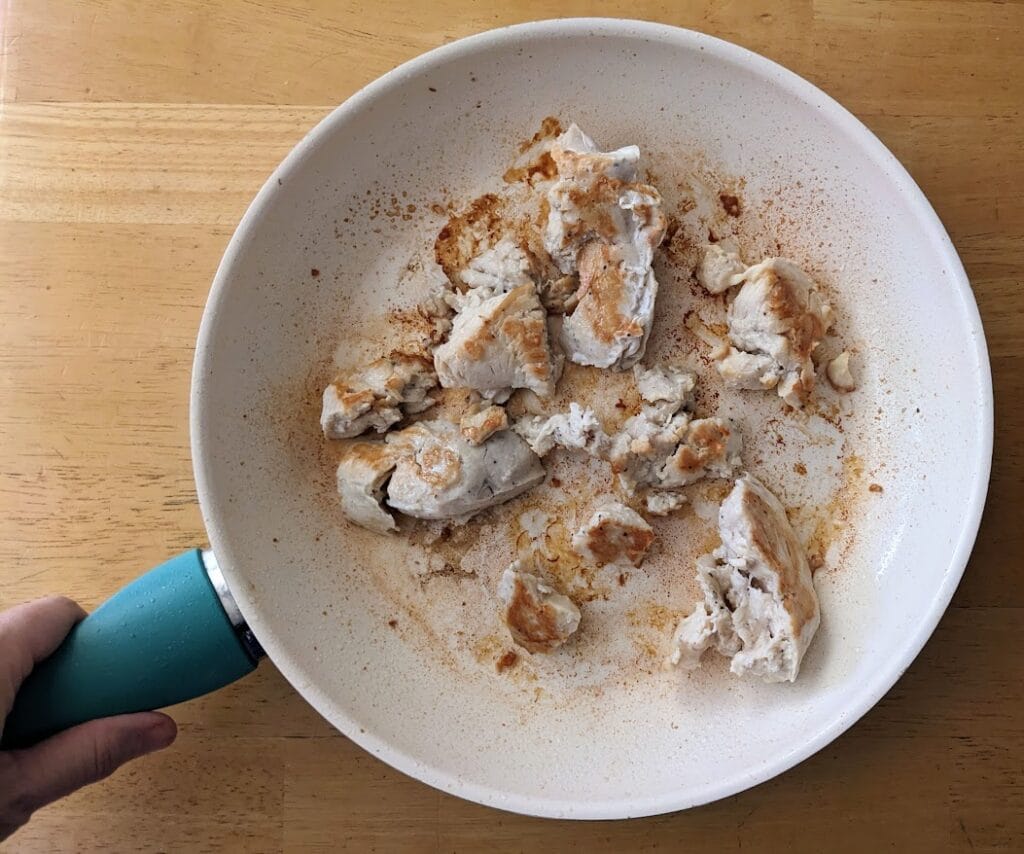 A hand holding a skillet with browned meat from Kevin's Thai Coconut Chicken Curry paleo meal.