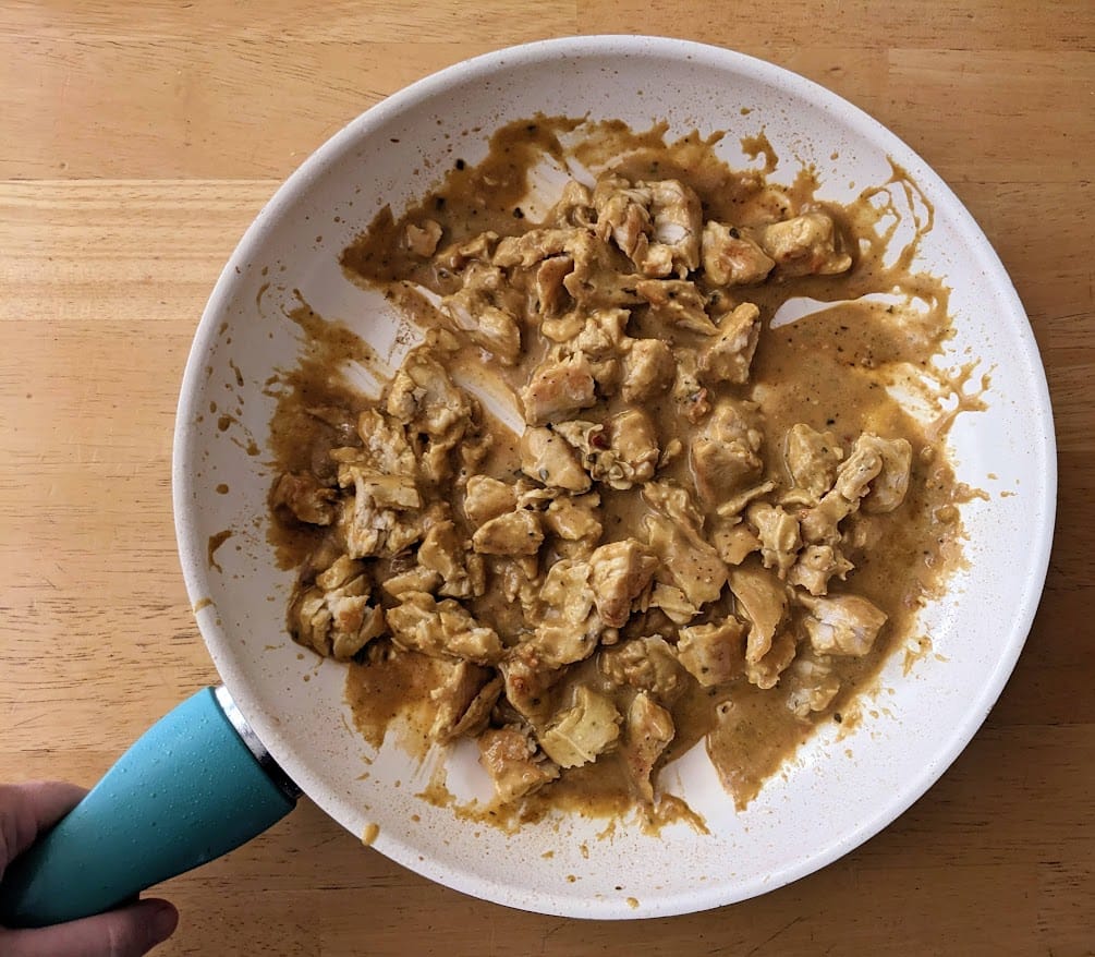 A hand holding a skillet with sauce and meat from Kevin's Thai-Style Coconut Chicken curry meal.