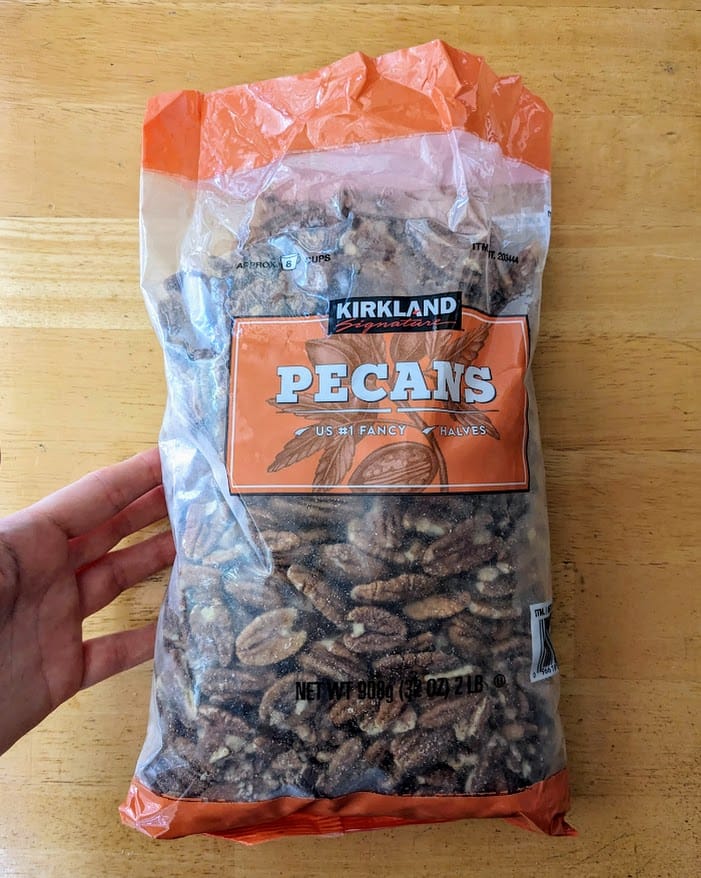 A hand holding a bag of Kirkland Pecan Halves from Costco.