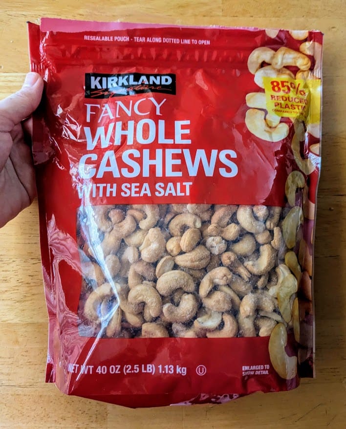 A hand holding a red bag of Kirkland Whole Cashews from Costco.