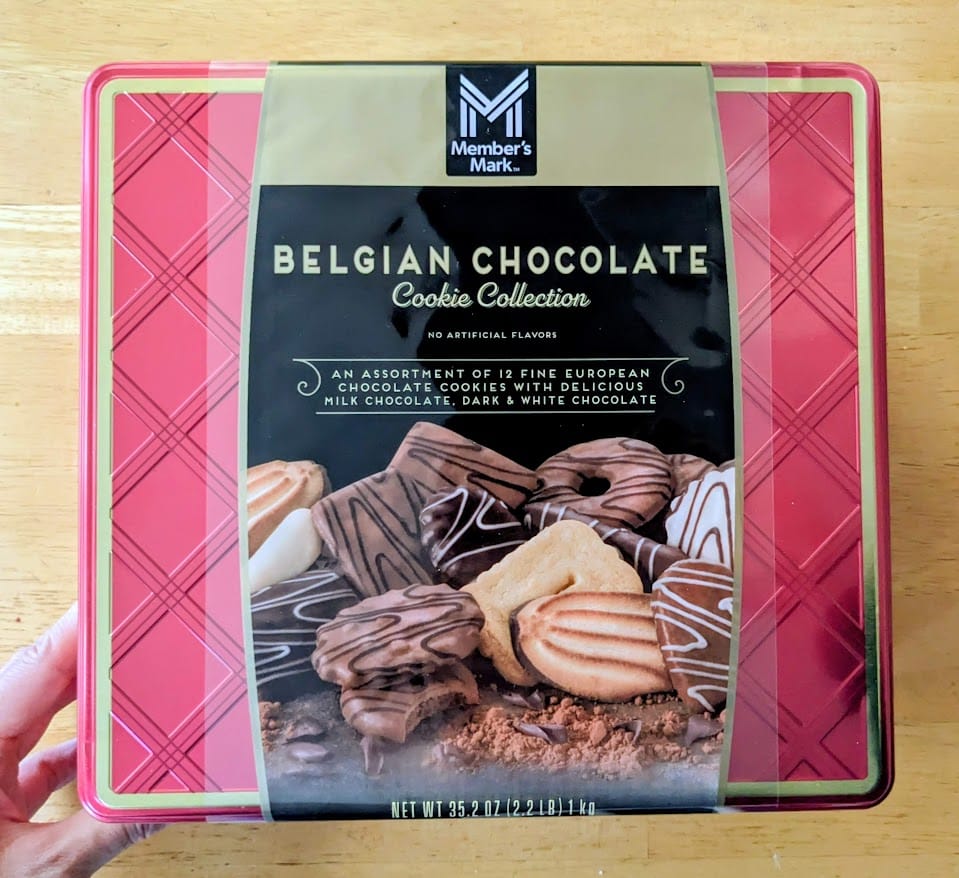 A hand holding a metal tin of Member's Mark Belgian Chocolate Cookies from Sam's Club.