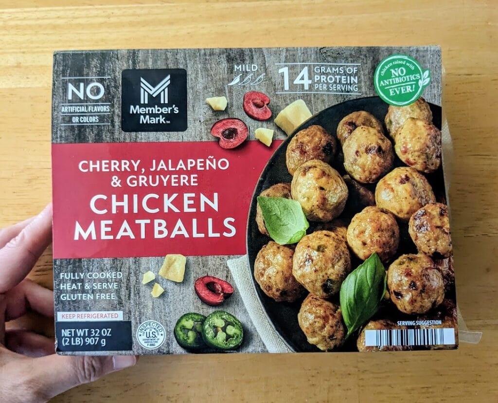 A hand holding a package of Member's Mark Cherry, Jalapeno, and Gruyere Chicken Meatballs from Sam's Club.