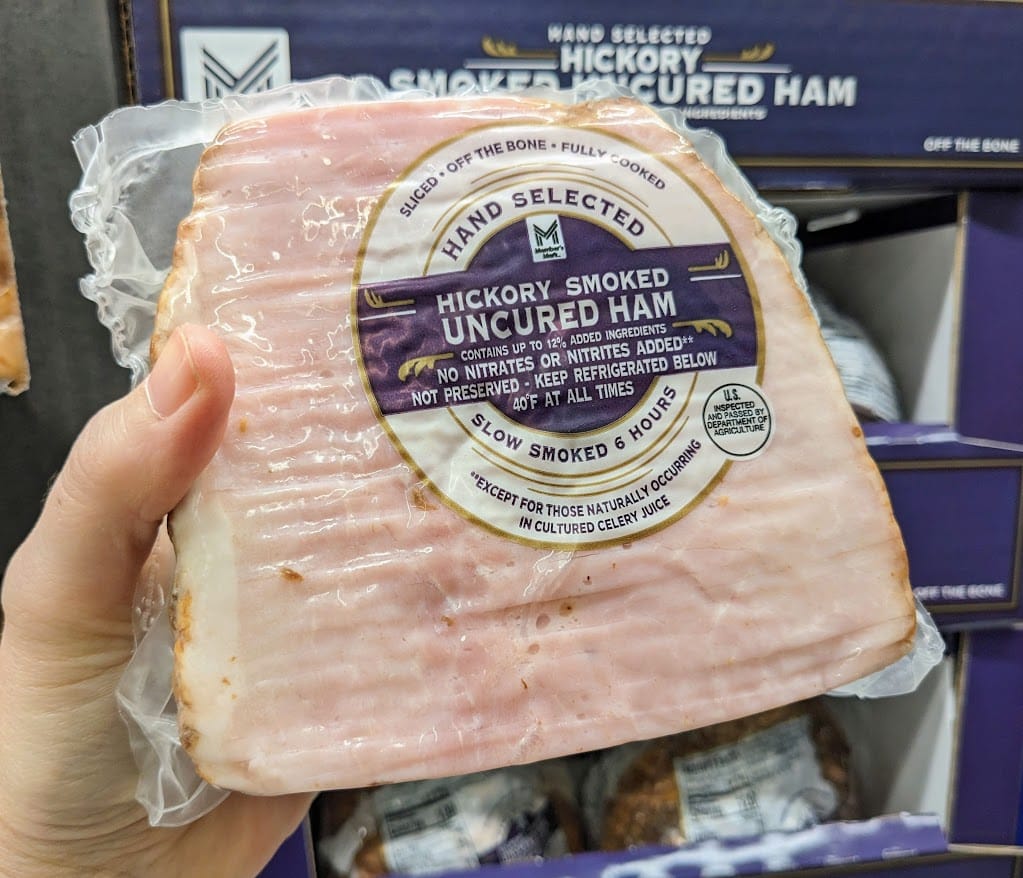 A hand holding a Hickory Smoked Uncured Ham inside a Sam's Club.
