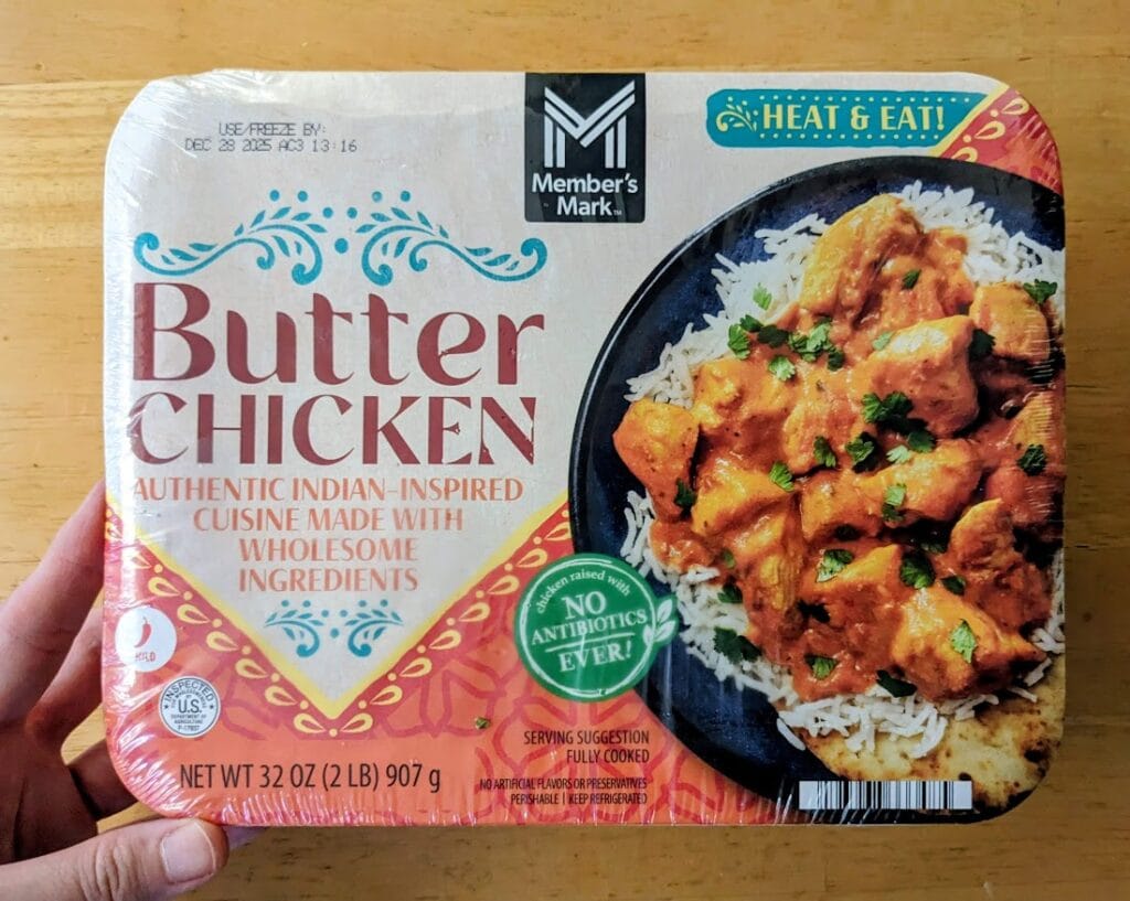 A hand holding a Butter Chicken Indian Curry meal from Sam's Club.