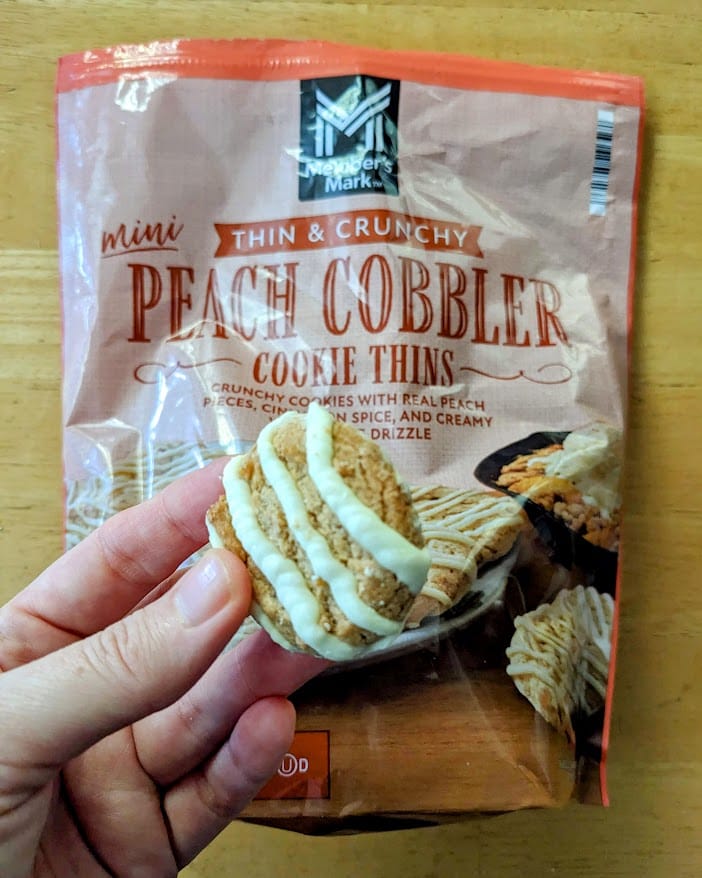 A hand holding a Peach Cobbler Cookie Thin over the bag from Sam's Club.