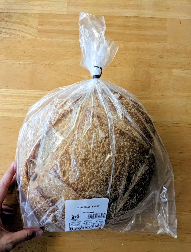 A hand holding a loaf of sourdough bread from a Sam's Club Bakery.